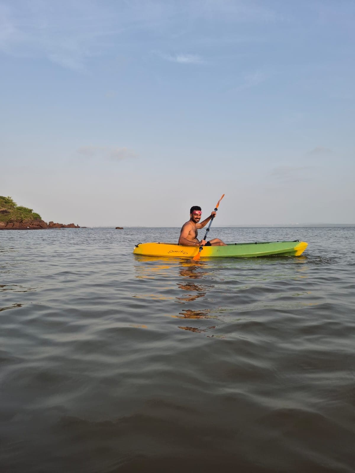 A swimmer paddling a kayak on calm water near Dona Paula
